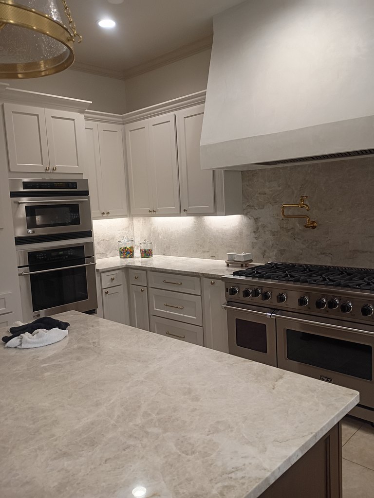 Refinished cabinetry against a marble backsplash and brass pot filler